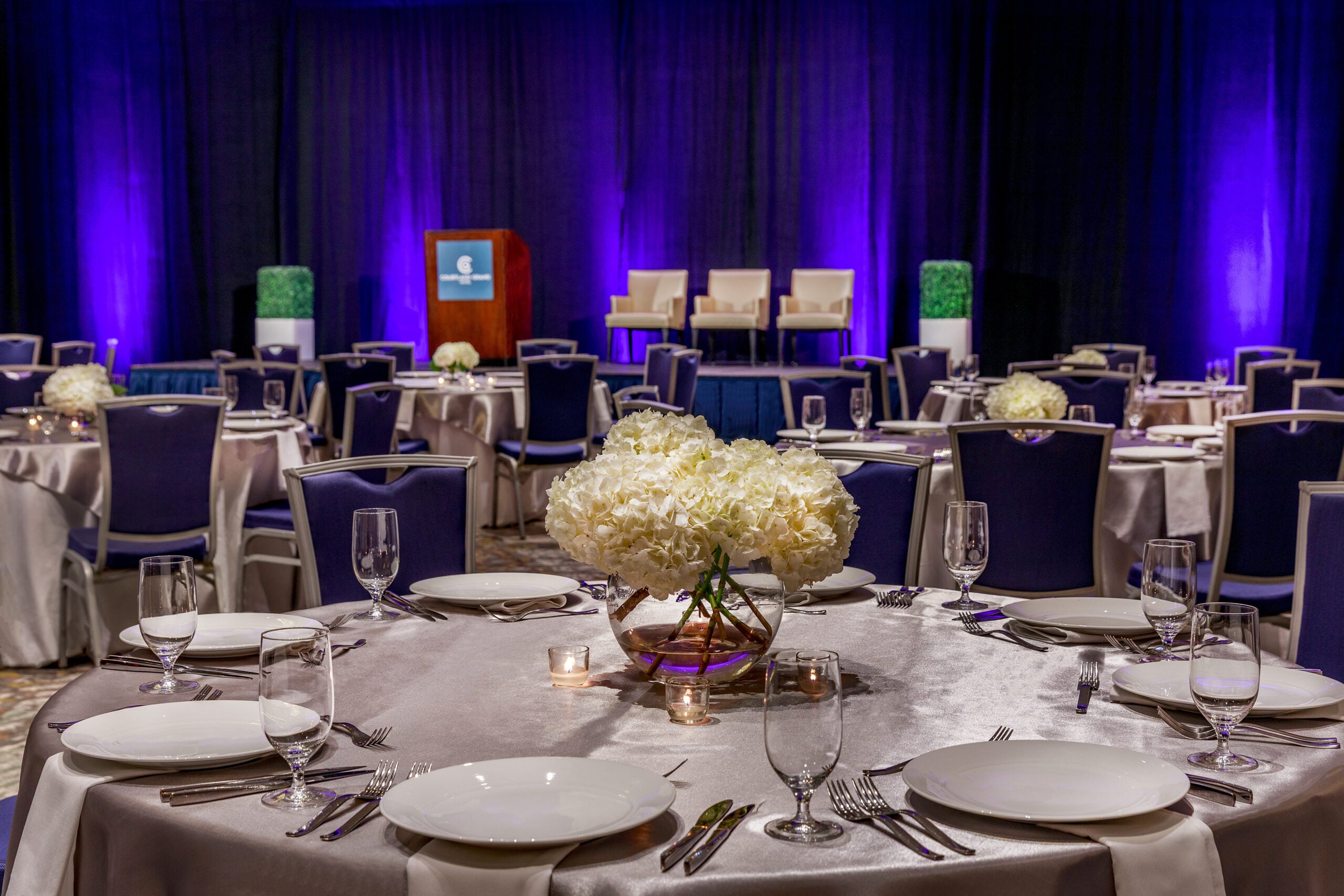 Detail of a Capitol Ballroom table — silver linens, white hydrangeas, candle centerpiece, purple uplit stage